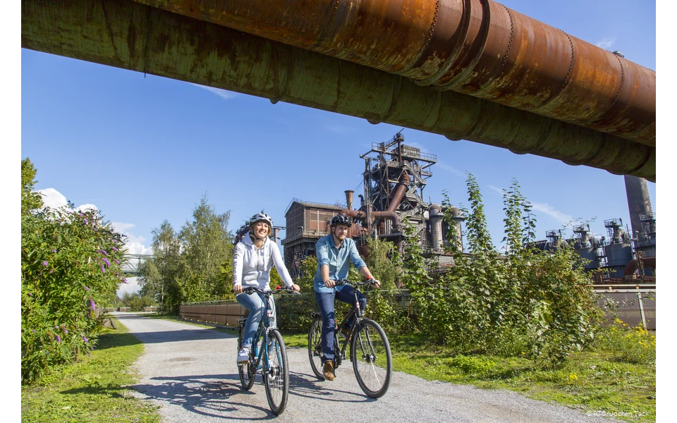 Zwei Radfahrer im Landschaftspark Duisburg bei blauem Himmel.