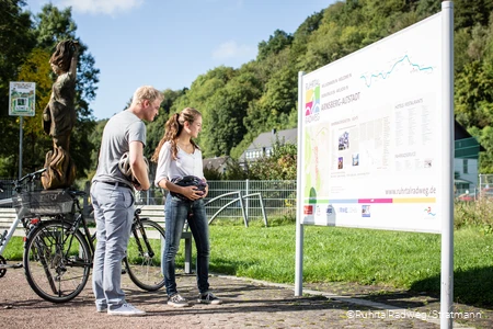 Paar mit Fahrrädern vor einer Stadtinformationstafel auf dem RuhrtalRadweg in Arnsberg