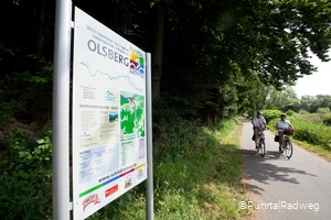 Stadtinformationsschild in Olsberg auf dem RuhrtalRadweg, an dem ein Paar auf Fahrrädern vorbei fährt